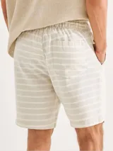 Bermuda de tela texturizada con diseño de rayas horizontales en color beige y blanco, con cintura elástica y cordón ajustable.