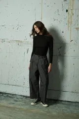 Pantalón de corte holgado y tiro alto en color gris oscuro, con pinzas frontales y costuras verticales decorativas a lo largo de las piernas.