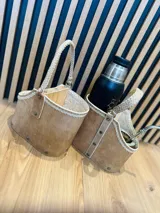 Cesto organizador de cuero color marrón claro con manija superior trenzada y detalles de costura en color crudo.