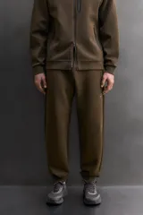 Pantalón jogger de entrenamiento, corte regular fit, color verde oliva oscuro. Confeccionado en tejido técnico compacto de algodón con elasticidad y efecto neopreno. Presenta cintura elástica ajustable con cordón blanco, bolsillos frontales y un bolsillo lateral con cierre de cremallera. El bajo termina en puño.