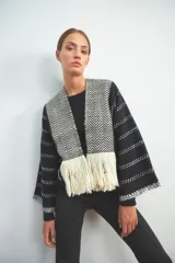 Chaqueta de punto en color negro con detalles en blanco, de frente abierto y diseño holgado. Presenta paneles frontales con patrón de zigzag y terminación de flecos en el ruedo, mientras que las mangas exhiben un motivo de líneas punteadas horizontales.