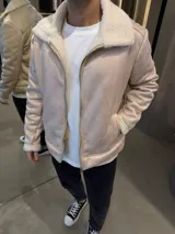 Campera de gamuza sintética color beige con interior y cuello de corderito blanco. Presenta cierre frontal metálico y bolsillos laterales.