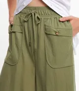 Pantalón pantacourt verde oliva de cintura alta con elástico, bolsillos laterales y lazo ajustable en la cintura.
