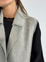 Chaleco largo color beige, con cuello solapa, un botón frontal y dos bolsillos de parche. Presenta costuras decorativas en contraste.