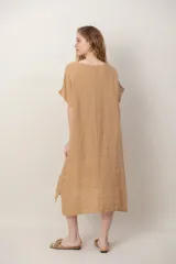 Vestido midi de lino color beige, de corte holgado y silueta acampanada. Cuenta con cuello redondo, mangas cortas amplias, bolsillos laterales y detalles de recortes horizontales en la falda con terminación asimétrica más larga en la parte trasera.