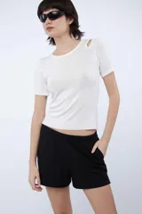 Top de punto blanco de manga corta, con diseño ajustado al cuerpo, cuello redondo y detalle de abertura en el hombro.