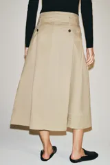 Falda midi color beige confeccionada en hilatura con mezcla de algodón. Presenta tiro medio, cintura con trabillas, bolsillos laterales ocultos en costura y cinturón del mismo tejido. Su diseño incluye un bajo acabado en línea evasé y cierre lateral con cremallera.