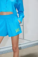 Short de poplín de algodón color azul vibrante, con cintura elástica ancha, bolsillos laterales y estampa de logo en color amarillo neón en el lateral izquierdo.