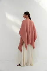Ruana de tejido de punto con textura, color rosa claro, con flecos en el ruedo. Diseño versátil y envolvente, ideal para usar como abrigo ligero.