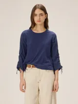 Blusa azul marino de manga larga con cuello redondo, confeccionada con delantero y mangas de lino, y espalda de algodón y spandex. Presenta detalles de fruncidos ajustables con cordones en las mangas.