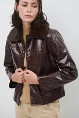 Chaqueta de efecto cuero brillante con acabado charol, cuello con solapas de piel sintética, cierre frontal con botones y bolsillos laterales.