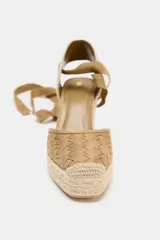 Sandalias de cuña color beige con capellada tejida y tiras de tela para atar al tobillo.