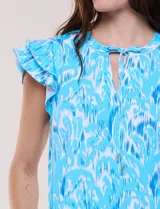 Vestido corto de playa con protección solar UPF 50, color celeste con estampado abstracto blanco y azul. Cuenta con escote en V con cordón ajustable, mangas cortas con volados dobles y prácticos bolsillos laterales.
