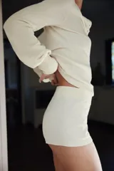 Mini shorts de punto color blanco, de tiro medio con cintura elástica y detalle de aplicación de botones en la parte delantera.