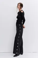 Pantalón de jean negro de corte recto y tiro alto, con detalle de botones metálicos plateados a lo largo de la costura lateral externa.