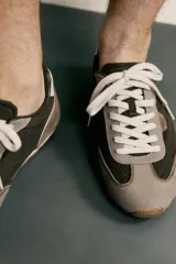 Zapatillas de estilo retro con cordones blancos, capellada marrón combinada con paneles de gamuza gris y detalles en cuero. Suela de goma a contraste.