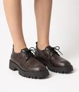 Mocasín dockside Satinato de color marrón oscuro, confeccionado en PU texturizado con efecto manchado. Presenta punta redondeada, costuras aparentes, ajuste frontal con cordones negros y una suela tractorada robusta de goma.