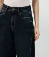 Pantalón de jean modelo new carrot, color azul oscuro, con tiro alto, cintura con pasantes, cierre frontal con botón y cremallera, bolsillos laterales y traseros, y detalles de tachas metálicas en forma de corazón.