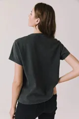 Remera gris oscuro de corte holgado, con cuello redondo y mangas cortas. Presenta un estampado frontal alusivo a Tom Petty and the Heartbreakers con motivos de corazón, guitarra y texto estilo vintage.