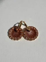 Aros tipo argolla dorados con dije redondo de resina color marrón brillante, bordeado con strass.