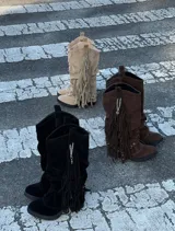 Botas de caña media confeccionadas en gamuza, con diseño holgado y detalle de flecos laterales con cadena metálica. Cuentan con suela plana y estilo western.
