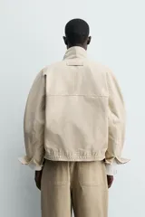 Cazadora regular fit de algodón color beige, con cuello subido y forro interior a cuadros. Presenta cierre frontal de cremallera oculta por solapa con botones a presión, bolsillos de vivo en la cadera y puños con botón.