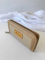 Billetera rectangular de cuero con cierre perimetral metálico. Presenta una textura grabada en el cuerpo central y un parche de cuero liso con el logo de la marca en la parte frontal.