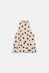 Top beige con estampado de lunares bordó, cuello halter, diseño sin mangas y bajo con volantes. Cuenta con cierre de lazada en la espalda.