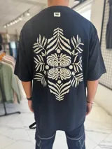 Remera oversize blanca con gran estampado en la espalda de diseño floral simétrico en tono oscuro. Cuenta con mangas cortas y calce holgado.