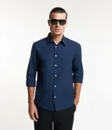 Camisa de hombre color azul marino, de corte regular, con cuello inglés y mangas largas que se pueden llevar remangadas. Presenta abotonado frontal con botones blancos.