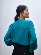 Blusa turquesa de mangas largas con puños fruncidos, cuello mao y detalle de frunces en el canesú.