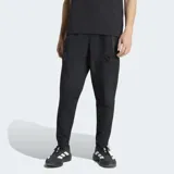 Pantalón deportivo Adidas del Real Madrid, modelo Tiro Travel, color negro. Presenta un diseño técnico con corte clásico, cintura elástica, costuras ergonómicas para mayor movilidad y bolsillos laterales. Incluye el escudo del club y el logo de la marca en tono sobre tono.