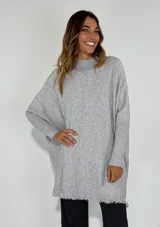 Sweater gris de punto, corte holgado, cuello alto y mangas largas con puños acanalados. El dobladillo inferior tiene un acabado deshilachado.
