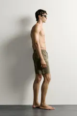 Short de baño largo en color beige, confeccionado en tejido técnico con tacto aterciopelado. Cuenta con cintura elástica ajustable con cordón, bolsillos laterales y detalle de bolsillo trasero, además de forro interior.