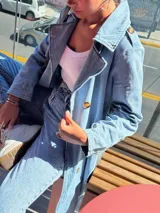 Trench de jean largo con diseño relajado, cuello solapa, cierre frontal con botones y charreteras en los hombros.