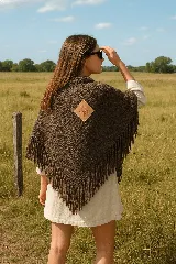 Chal marrón de tejido grueso con flecos en el borde inferior y parche de cuero con diseño de sol en la espalda.