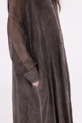 Vestido camisero largo, color gris oscuro con efecto desgastado/lavado. Presenta cuello camisero, botones frontales y mangas largas. El bajo es irregular y se superpone con un forro o capa de tela negra con terminación de encaje o volado.