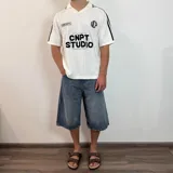 Chomba de tejido de punto color negro, con cuello polo y cierre frontal parcial. Presenta diseño de rayas verticales sutiles en el tejido, detalles de líneas blancas en los hombros y estampado frontal con texto y gráficos en color blanco.