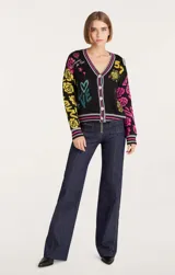 Cárdigan de punto negro con cuello en V y cierre frontal con botones. Presenta estampado de flores, corazones y números en colores amarillo, rosa y verde.