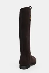 Bota de caña alta confeccionada en serraje, con diseño de estilo hípico. Presenta detalle de pespuntes verticales, tira decorativa con hebilla metálica en la parte superior de la caña y puntera redonda. Cuenta con suela plana de 2,5 cm y sistema de calce tipo pull-on.