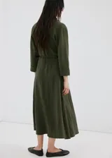 Vestido largo verde militar, con cuello camisero, cierre frontal con botones, mangas tres cuartos y diseño evasé. Incluye un cinturón fino de poliuretano con hebilla metálica.