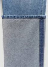 Pantalón de jean de corte recto y tiro medio, confeccionado en algodón. Presenta un diseño distintivo con el bajo vuelto en un tono de denim más claro y una costura lateral vertical en contraste.