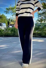 Pantalon de corte wide leg color negro con una franja vertical blanca lateral. Presenta un diseño de tiro alto y silueta fluida.
