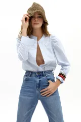 Camisa de popelina de algodón con estampado de rayas verticales celestes y blancas. Presenta cuello mao, cierre frontal con botones de nácar, mangas largas con hombros ligeramente fruncidos y abullonados, y detalles de corazones bordados y aplicados en el frente.