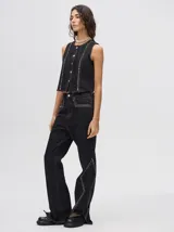 Pantalón de jean tiro alto con corte ochentoso y terminación oxford. Presenta apliques metálicos decorativos alrededor de los bolsillos delanteros y traseros, y a lo largo de la parte externa de las piernas.