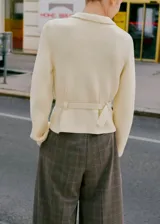 Cardigan de punto color marfil, de tejido de punto medio, con cuello camisero, cierre frontal de cremallera, manga larga y cinturón incorporado con hebilla.