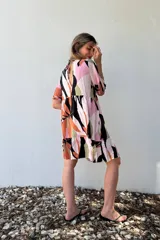 Vestido corto con volados, estampado con formas abstractas en tonos naranja, rosa, negro y verde.