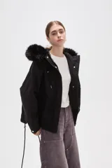 Campera negra de algodón con capucha, cierre frontal oculto y bolsillos laterales. Presenta un diseño holgado con detalles de piel sintética en el borde de la capucha.
