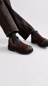 Bota tipo chelsea de punta redonda, confeccionada en una combinación de cuero y gamuza en tonos marrones, con elásticos laterales y suela de goma track con plataforma.