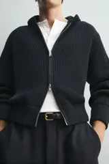 Chaqueta de punto compacto con capucha, confeccionada en hilatura con lana. Presenta cierre frontal con cremallera, mangas largas y acabados en rib.